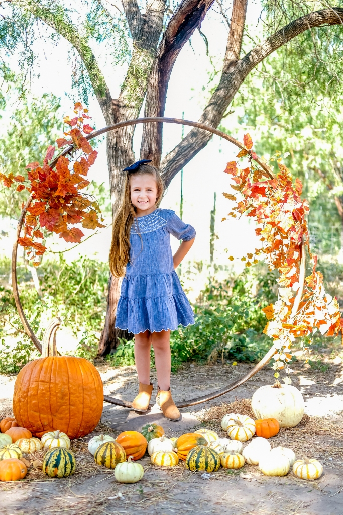 A young girl wearing a blue dress poses for her fall photos at Maddie's Pumpkin Patch.
