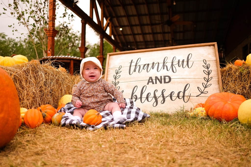 A baby sits on a plaid blanket as she poses for a photo at Maddies Pumpkin Patch in McAllen, Texas